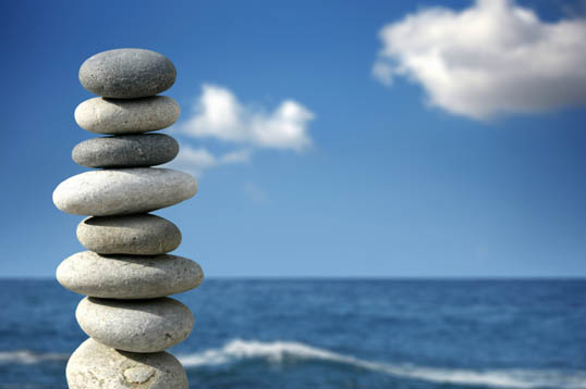 Photograph of a number of flat stones piled carefully onto another with a fantastic bright blue sky background at the seaside.